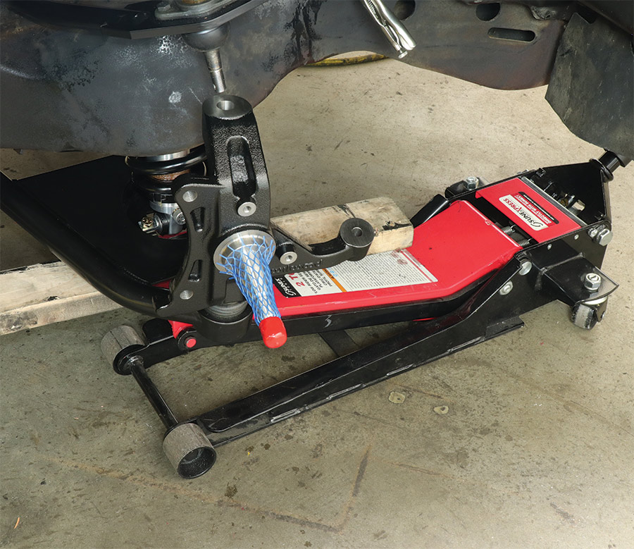 A floor jack under the lower control arm working to compress the Aldan coilovers