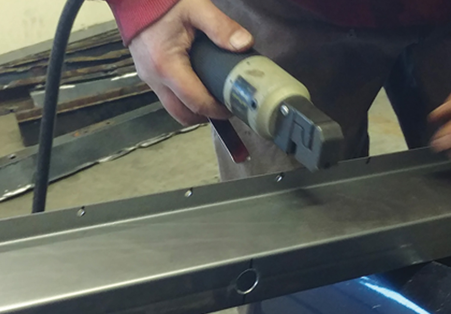 mechanic uses a pneumatic punch tool to put holes in the new crossmembers