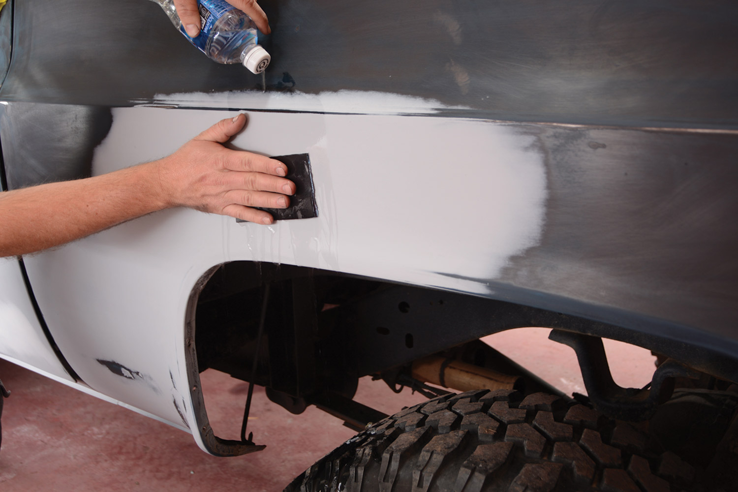 mechanic uses 320-grit wet-or-dry sandpaper to sand the back driver side