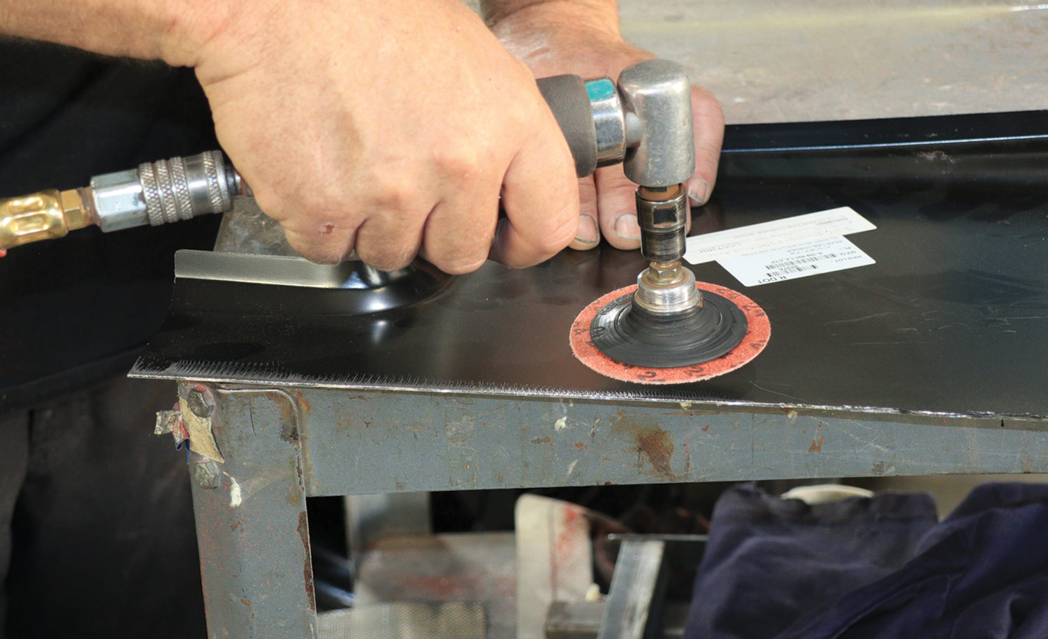 mechanic uses a 24-grit sanding disc to smooth the metal’s rough edge