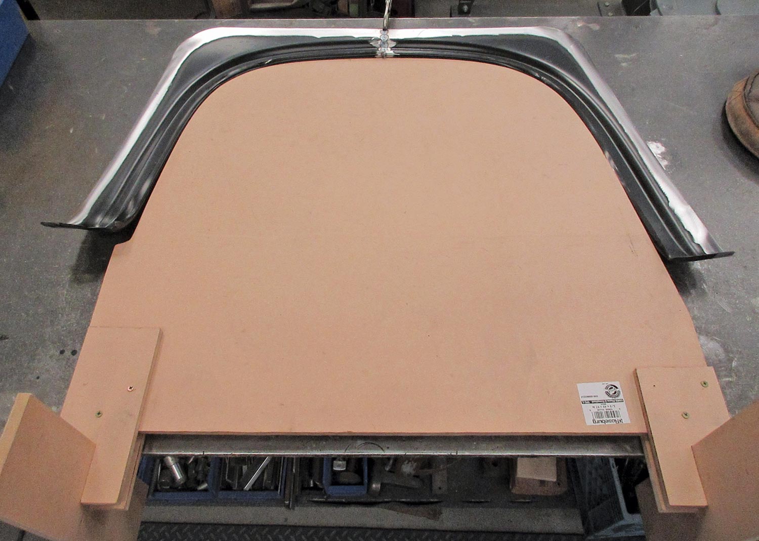 an MDF form created to transfer the size, shape, height, angle, and curvature of the wheelwell opening from one side to the other, sits on a counter with a fender part