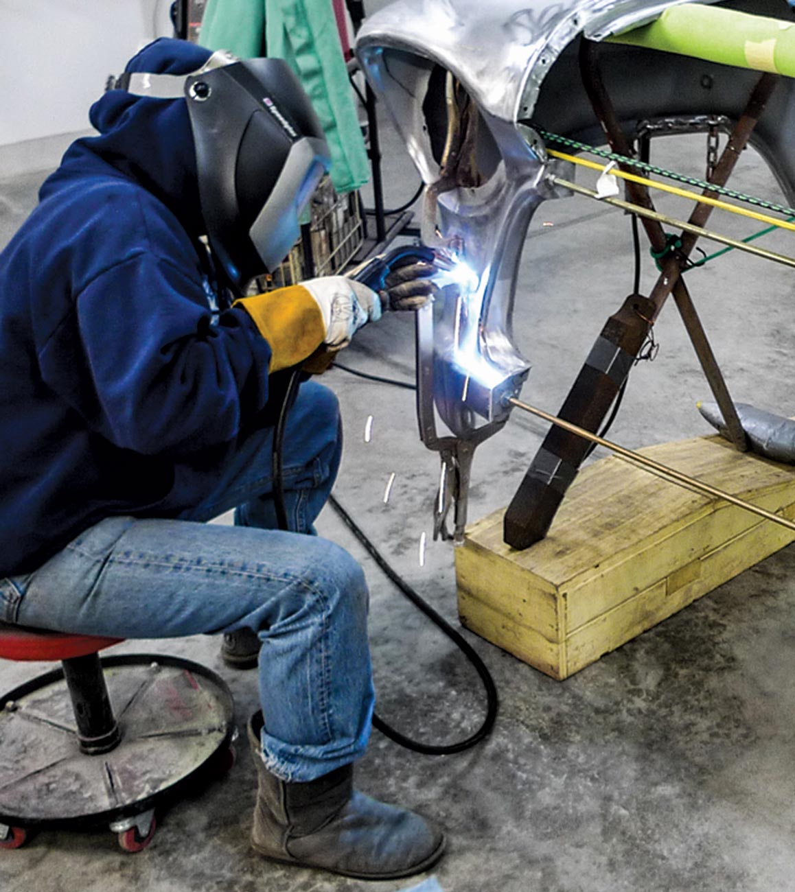 a mechanic, in full coverage clothing and wearing a mask, welds the slug to the fender