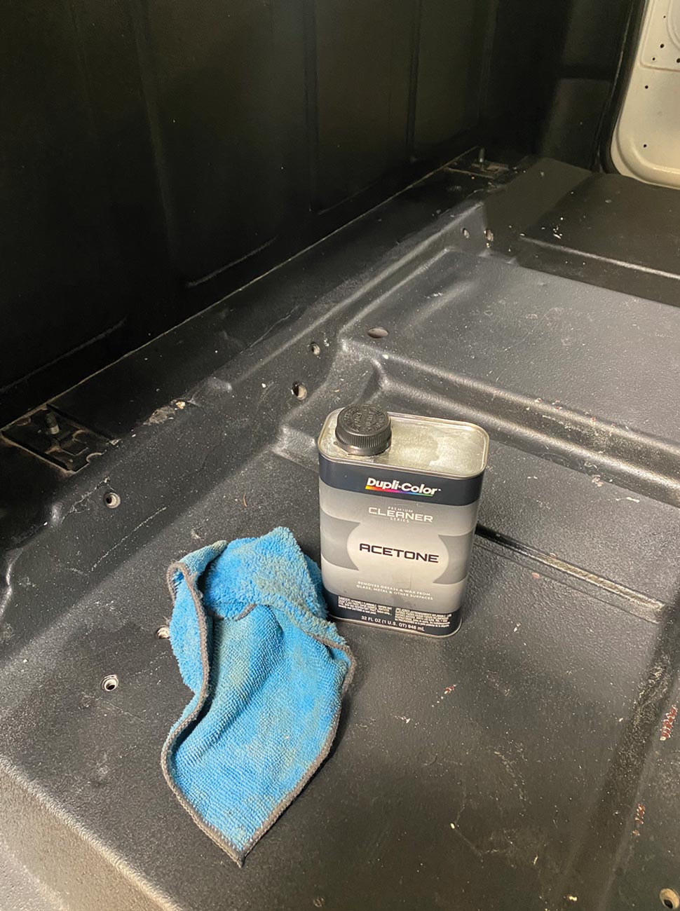 a container of acetone and a rag sit on the bare floor of the cab