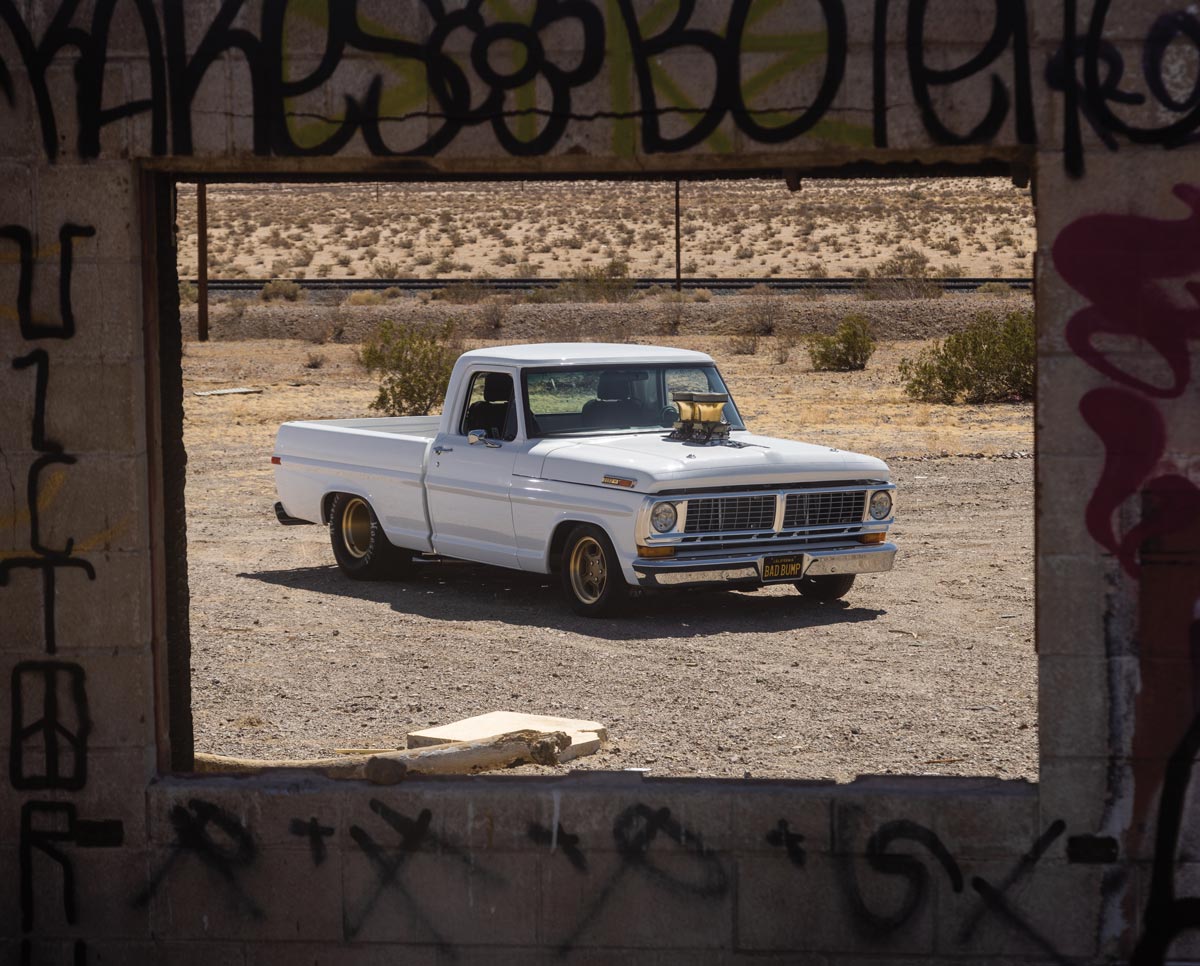looking at a white truck through a hole in a brick wall covered in graffiti