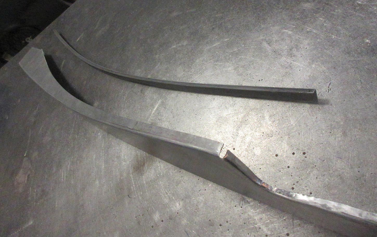 a bent strip of metal sits next to the first panel, both with matching contours