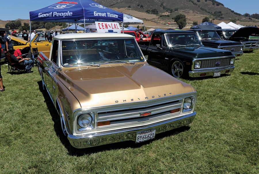 gold truck and black trucks parked on the grass at an event