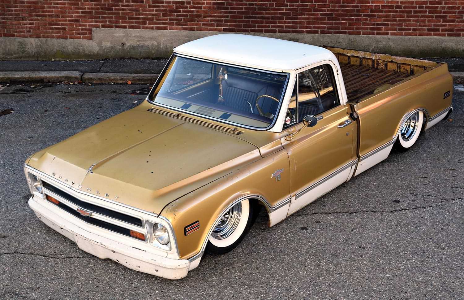 close birds eye view of the gold and ivory '68 C10 parked next to a red brick wall