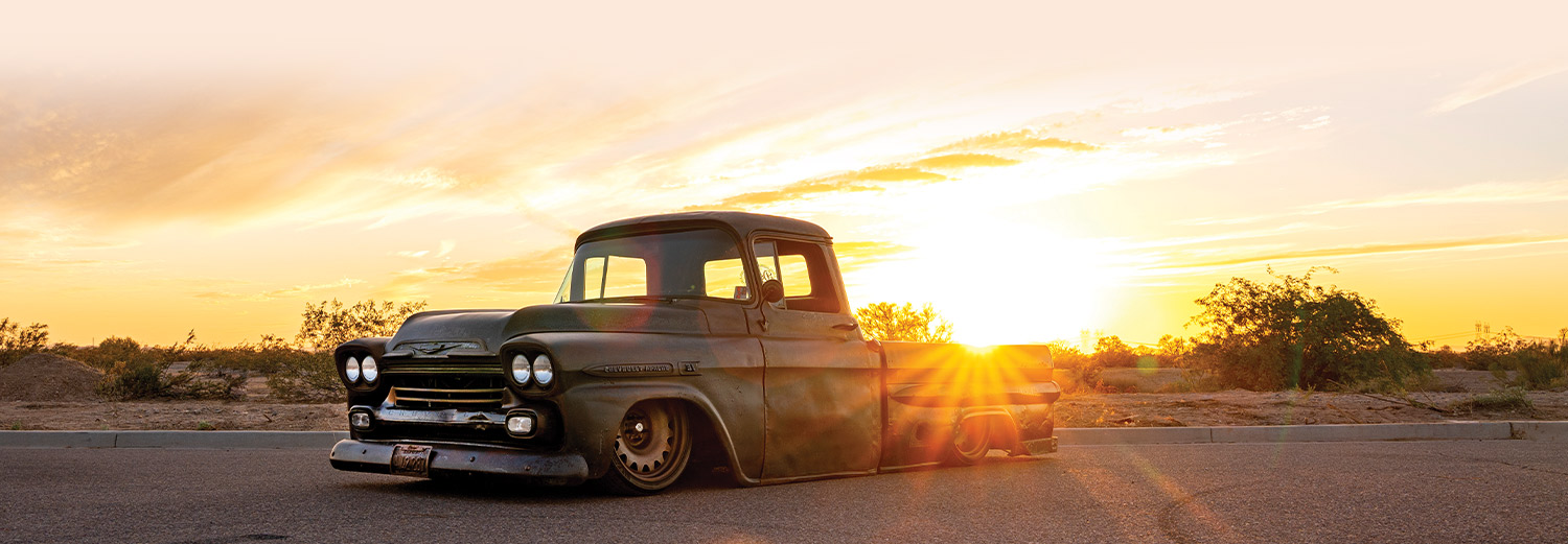 three quarter view of the '59 Apache parked in a desert area, against a bright yellow sunrise