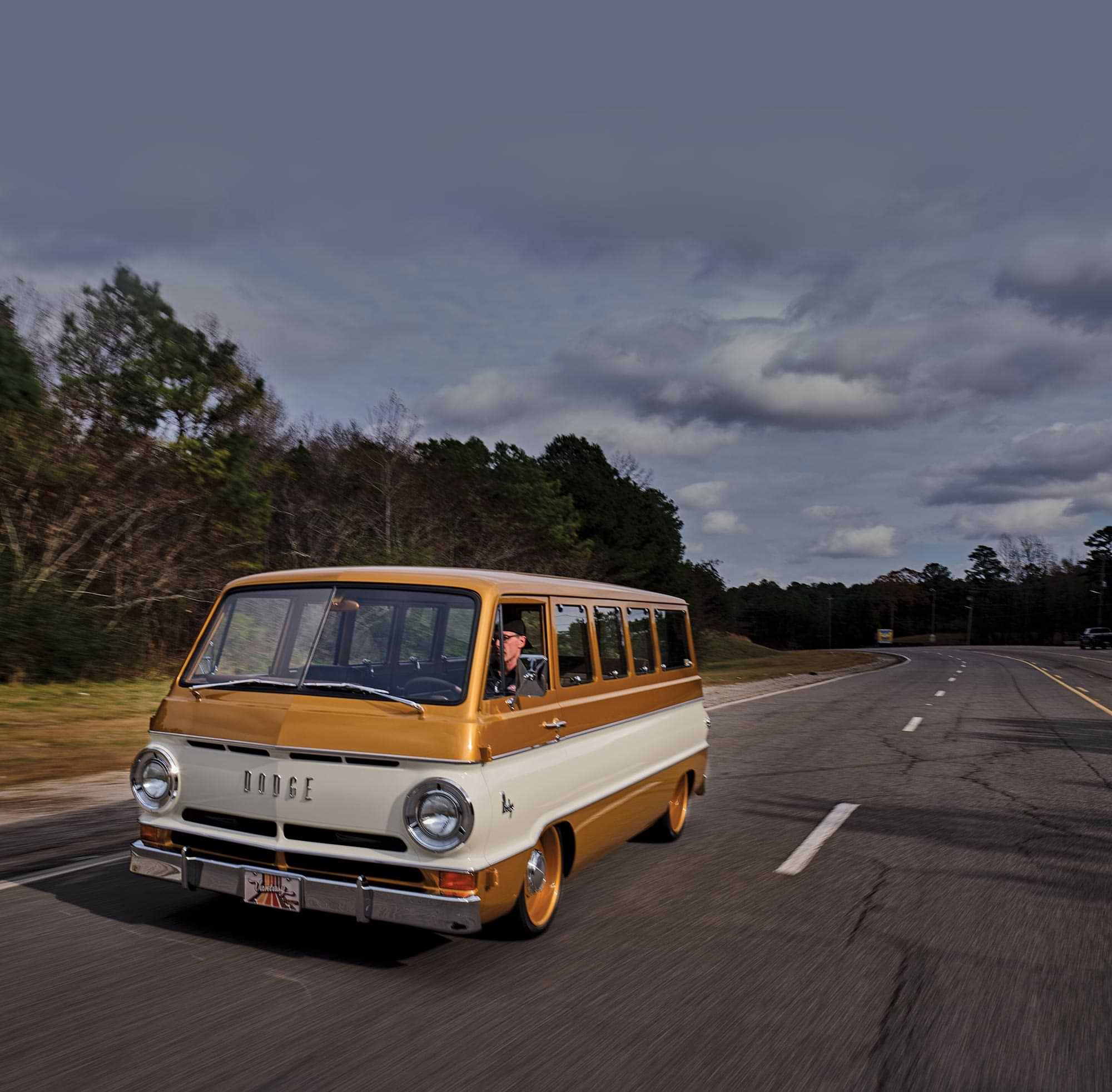 a man drives the vintage '69 Dodge A108 down a road on a cloudy day