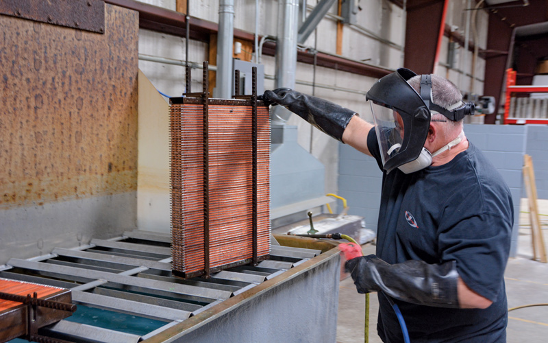 Special fixtures are used to hold the core before it is capped with the custom header panels, which are stamped in-house. Here, the cores are dipped in a heat-activated flux and lightly dried with an air nozzle.