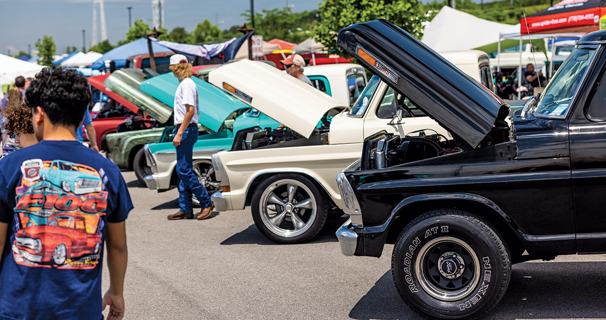 Close-up photograph perspective of nearby spectators walking alongside vintage Ford F-100 trucks at the 2023 Grand National F-100 Show in Pigeon Forge, Tennessee on a sunny/gloomy day