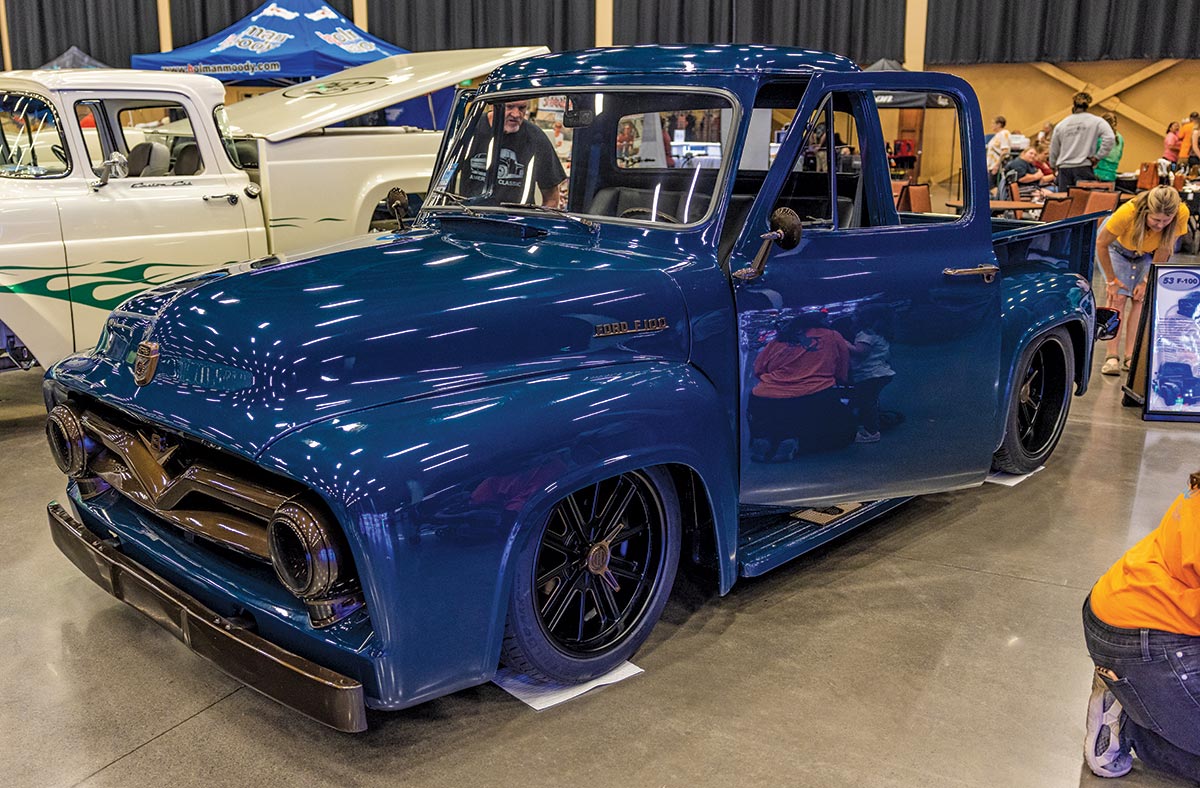 Close-up photograph perspective of a shiny vintage dark blue 1953 Ford F-100 car on display with the driver side door open for spectators to glance at inside the 2023 Grand National F-100 Show in Pigeon Forge, Tennessee