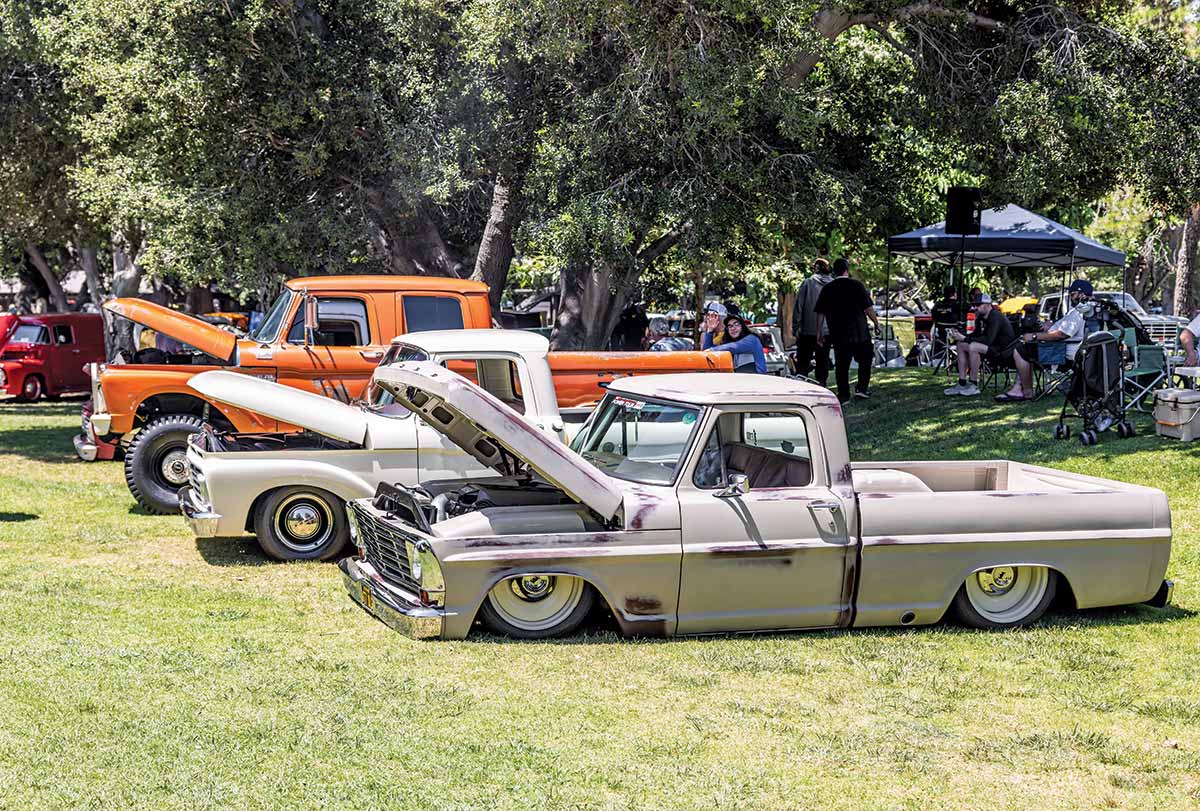 Landscape close-up photograph perspective of three vintage Ford vehicles parked next to each other on the grass with their front hoods open on display at Canyon RV Park in Anaheim, California