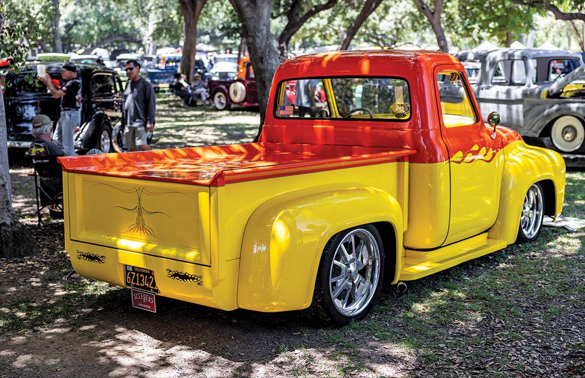 Landscape close-up photograph perspective of a red/yellow vintage Ford vehicle parked on display on the grass with other spectators nearby enjoying the day at Canyon RV Park in Anaheim, California