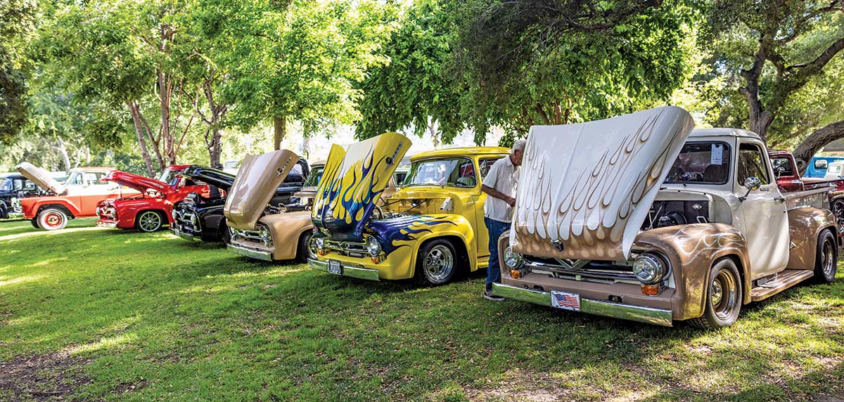Landscape close-up photograph perspective of six vintage Ford vehicles parked on display on the grass with their front hoods open at Canyon RV Park in Anaheim, California