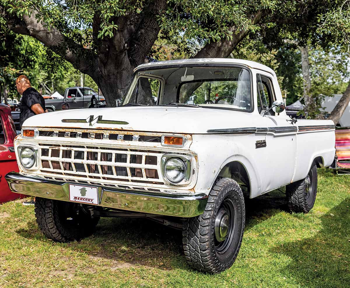 Landscape close-up photograph perspective of a white vintage Ford truck parked next to another vehicle as there is a spectator nearby looking at a different model at Canyon RV Park in Anaheim, California