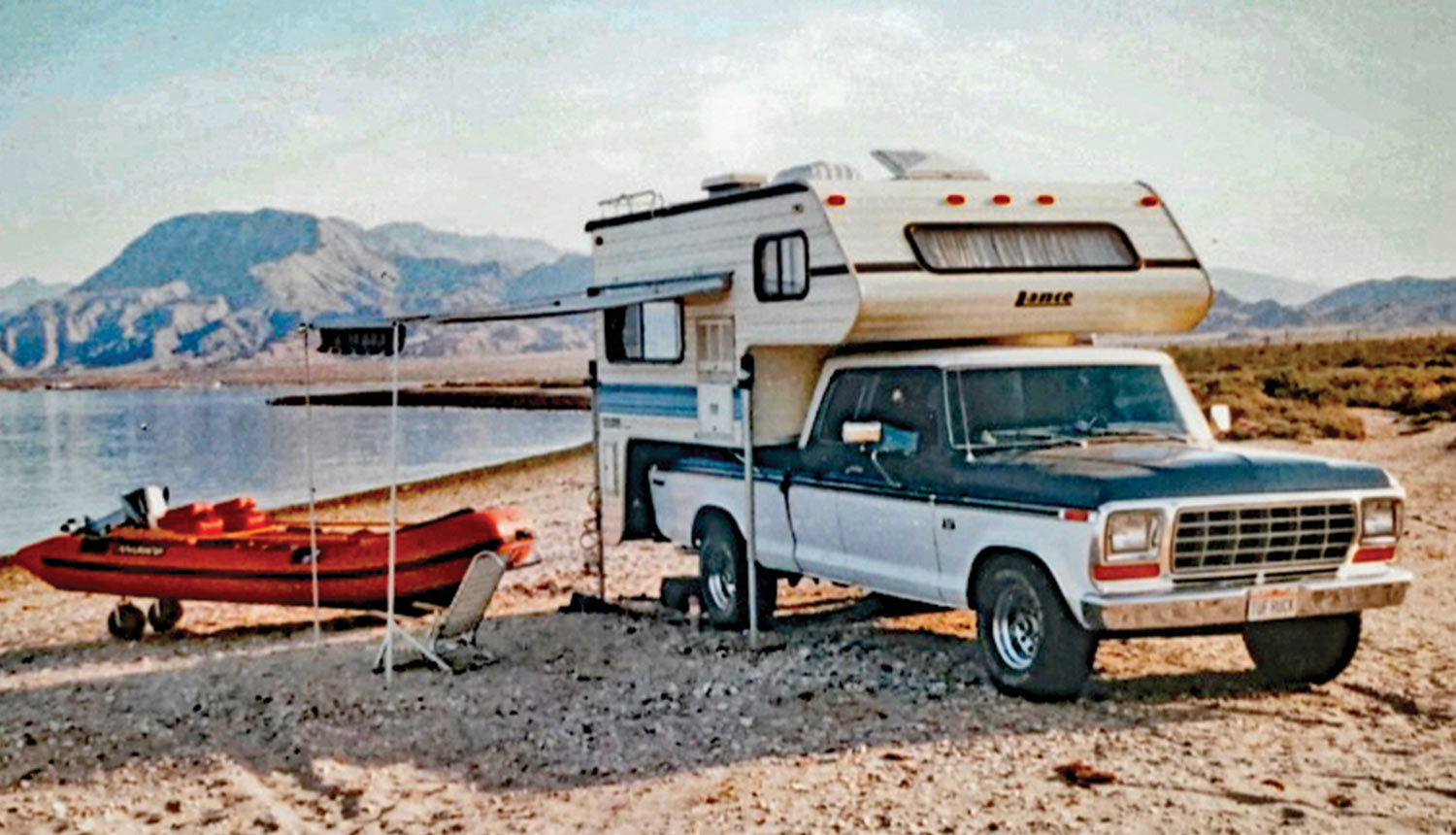 an old dated looking photo of the ’75 Ford SuperCab with a trunk trailer and a canoe connected, parked beside a lake