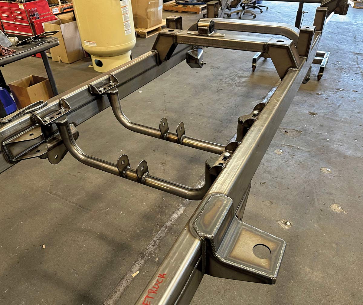 The tubular transmission and transfer case crossmembers bolt in. The brackets outside the frame are cab mounts, the raised brackets in the rear mount the pickup box.
