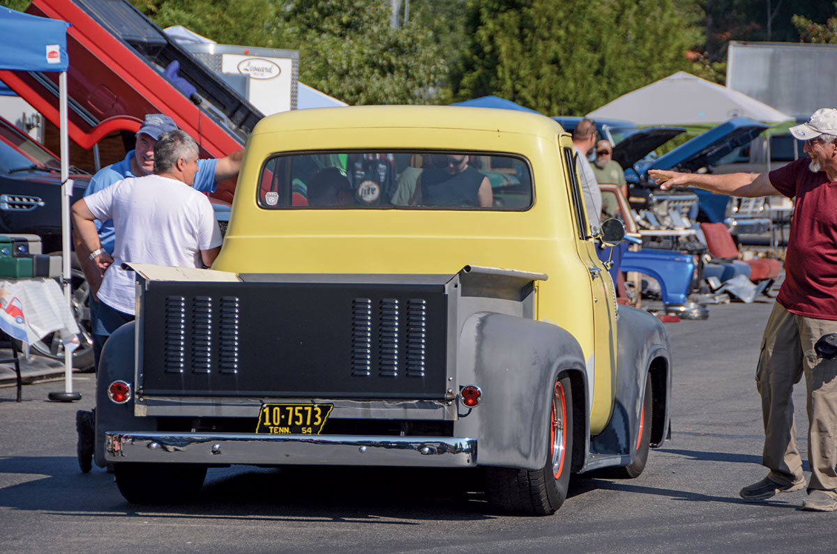 Close-up landscape photograph rear perspective of a yellow-colored Ford vintage vehicle with the black and yellow Tennessee license plate as there are other people standing next to the driver's side and another man is next to the passenger's side