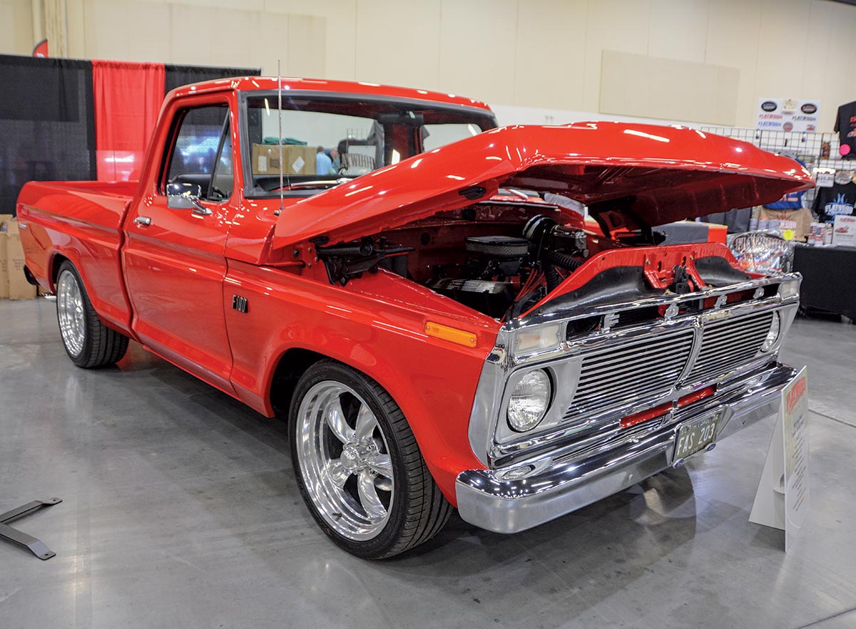 Close-up landscape photograph angle perspective of a shiny/glossy red-colored Ford vintage F100 vehicle with its hood open parked inside a showroom display area