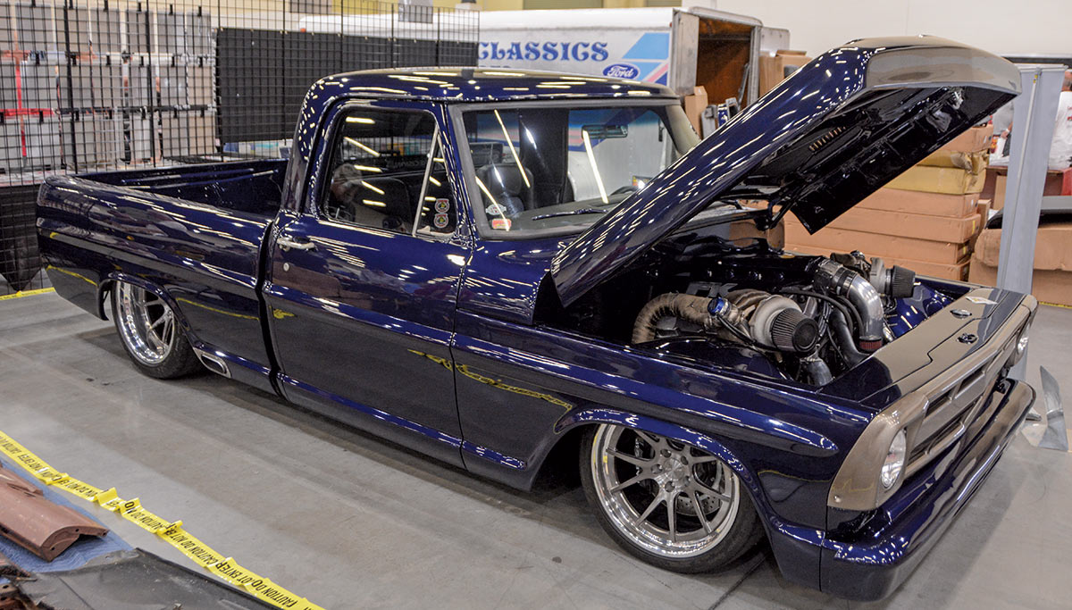 Close-up landscape photograph angle perspective of a shiny/glossy dark navy blue-colored Ford vintage vehicle with its hood open parked inside a showroom display area