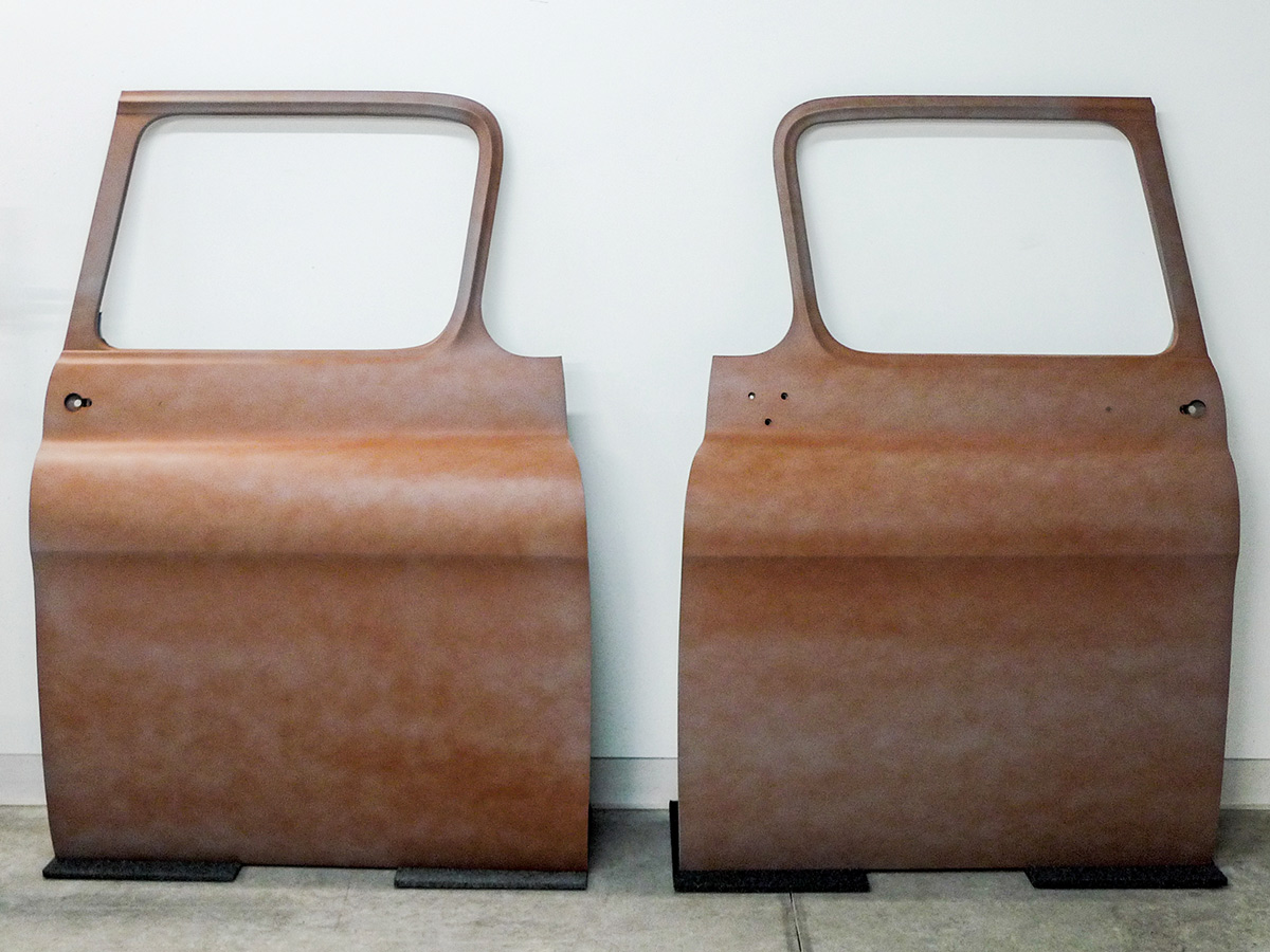 Two rusty car doors leaning against a white wall