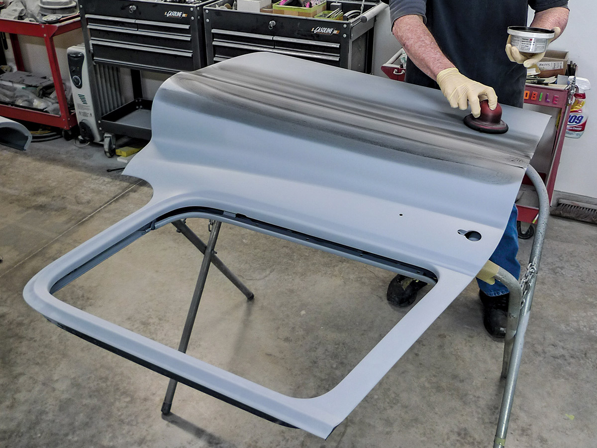 Man applying a dry guidecoat to the exterior of the unpainted car door that's laying on the stand