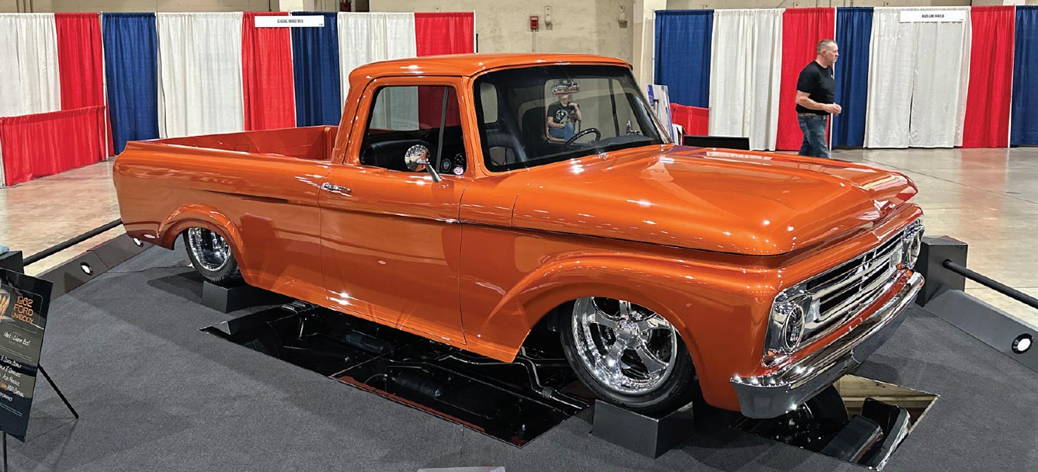 passenger side quarter view of an orange low riding classic truck on wheel stands