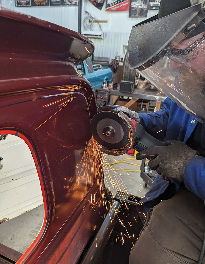 Man wearing a welding mask, using a small hand held saw to cut into the back of the truck