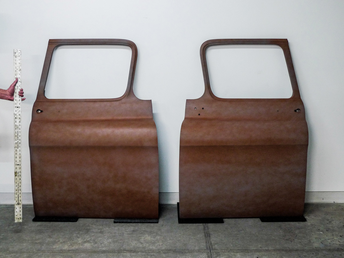 Two rusty car doors leaning against a white wall