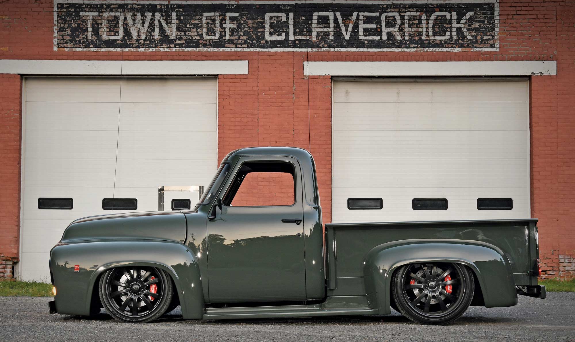 Side view of Dark green ’54 F-100 pickup truck parked in front of brick wall with painted sign reading Town of Claverack