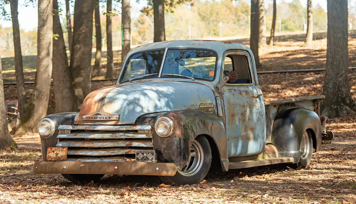 blue truck with bare trees in the back