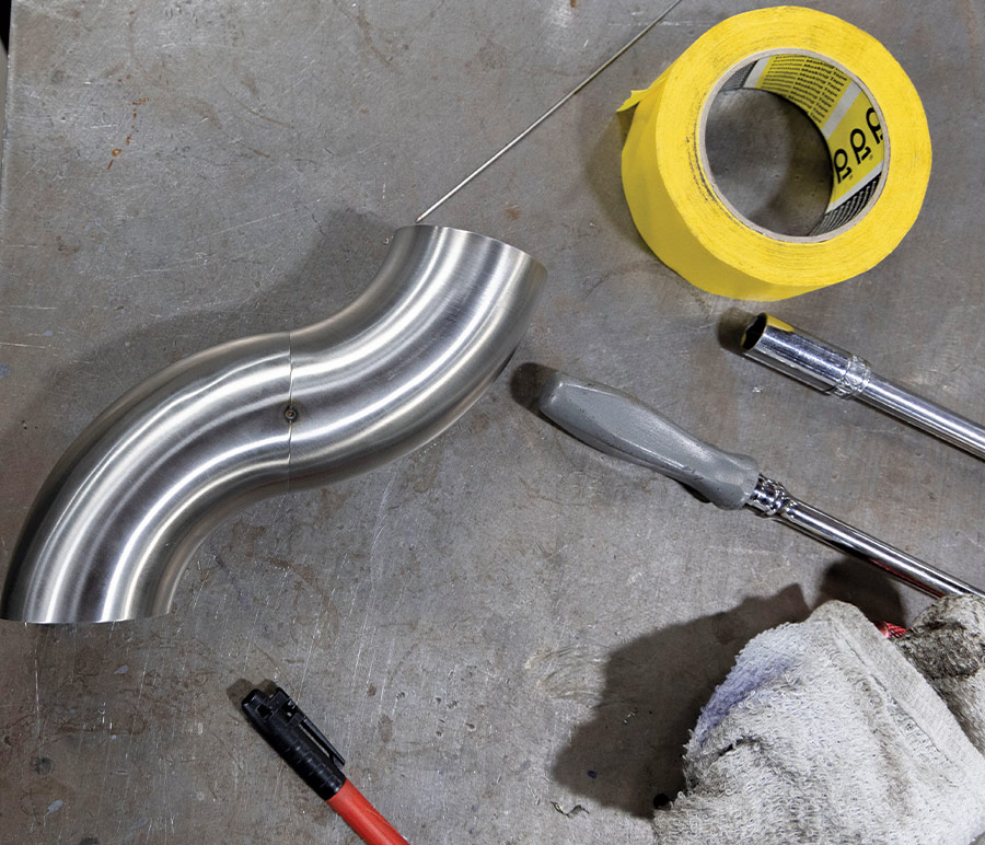 exhaust pipe on metal work table with roll of tape and tools surrounding it