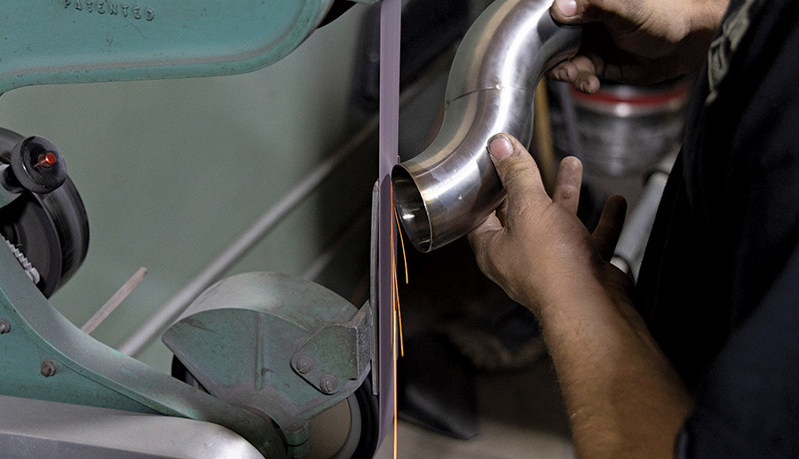 person holding up exhaust pipe against a polishing belt