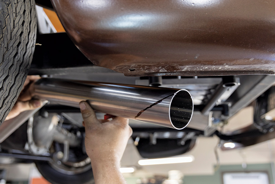 closeup of person fitting exhaust pipe underneath a car