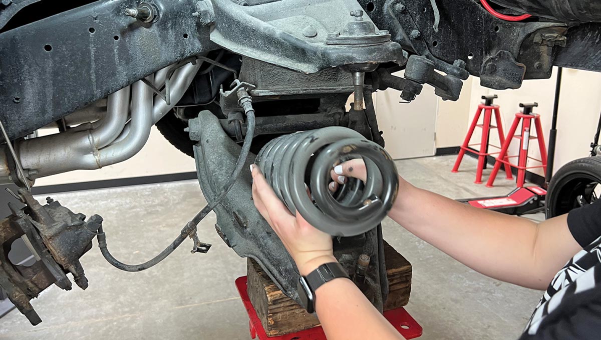 two hands carefully remove a coil spring from the lifted truck