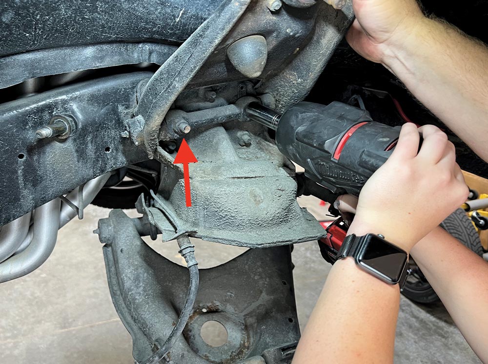 a red arrow points to one of two bolts to be removed from the chassis to release the upper A-arm