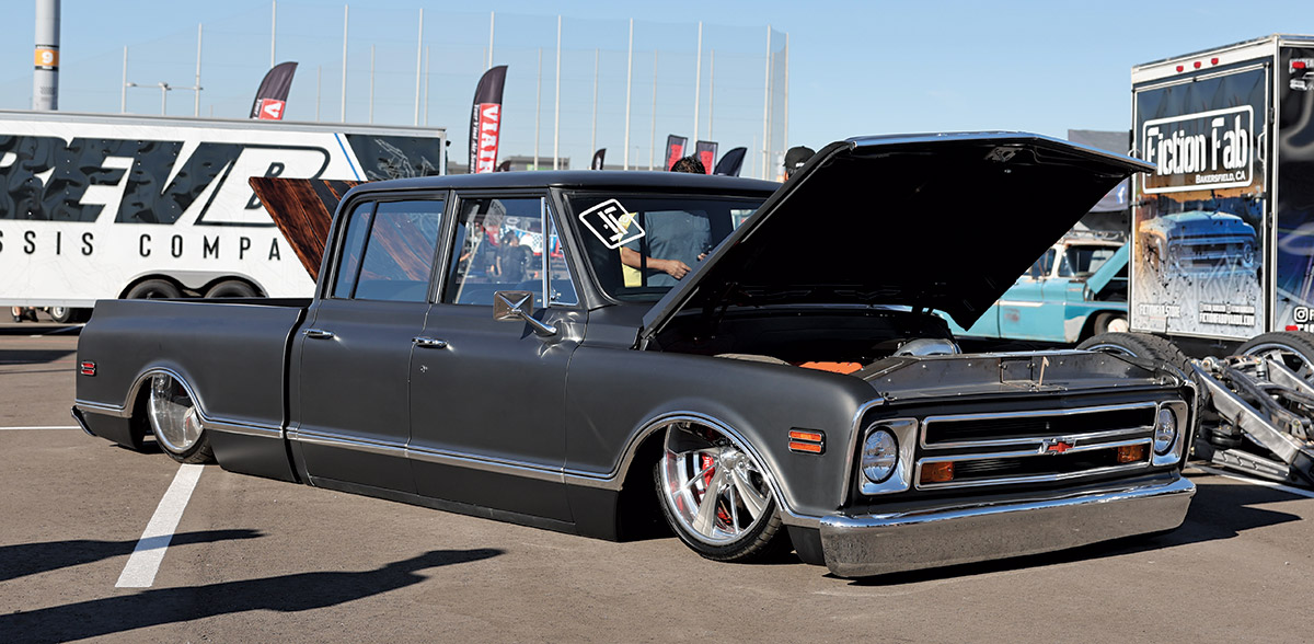 Close-up landscape photograph view of a black matte Chevrolet vintage truck vehicle parked in a parking lot space with its front hood slightly open