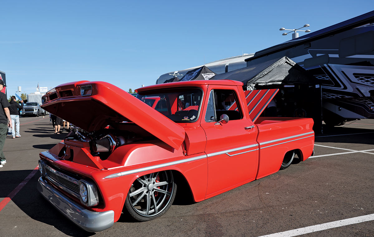 Close-up landscape photograph view of a red colored Chevrolet vintage truck vehicle that has its front hood slightly open and back trunk slightly open as the vehicle is parked in a parking lot space