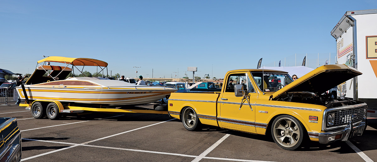 Close-up landscape photograph view of a yellow/golden colored Chevrolet vintage truck vehicle that has its front hood slightly open and pulling a pontoon motorboat vehicle trailer with the motorboat mounted on top