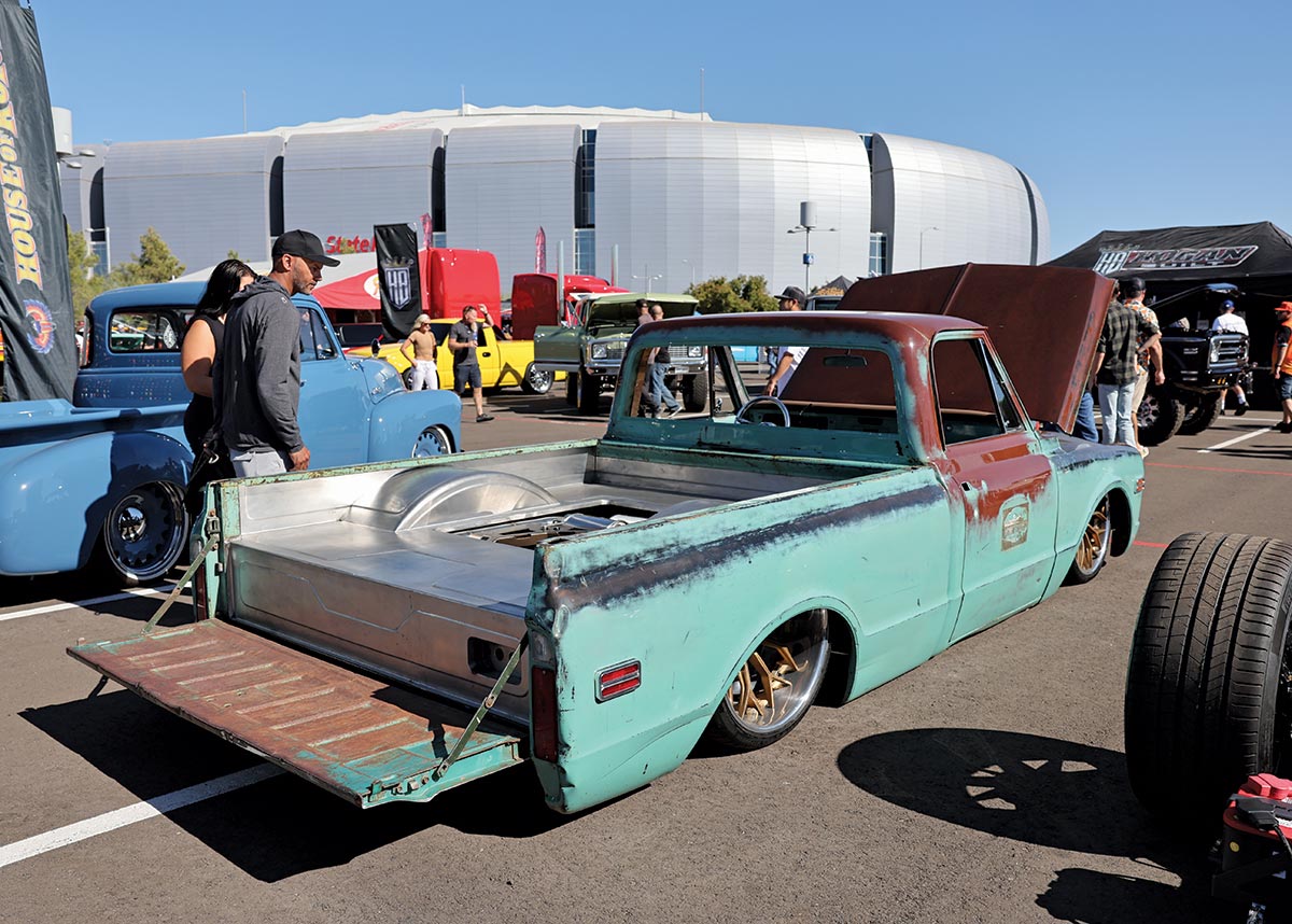 Close-up landscape rear photograph view of a rusty mint green/dark brown Chevrolet C10 vintage truck vehicle parked in a parking lot space area nearby the State Farm Stadium venue in Glendale, Arizona