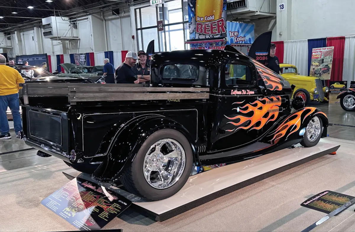 quarter passenger rear view of a black classic truck with front flames and dark wood truck bed side rails