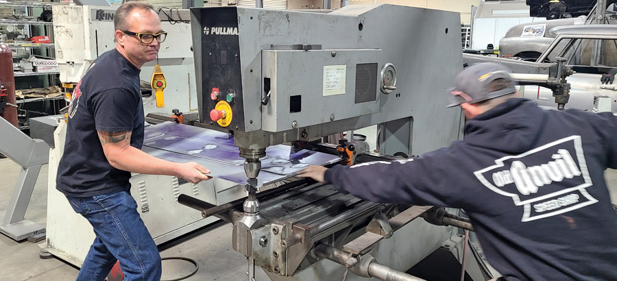 two men pushing a tailgate panel through a welding machine