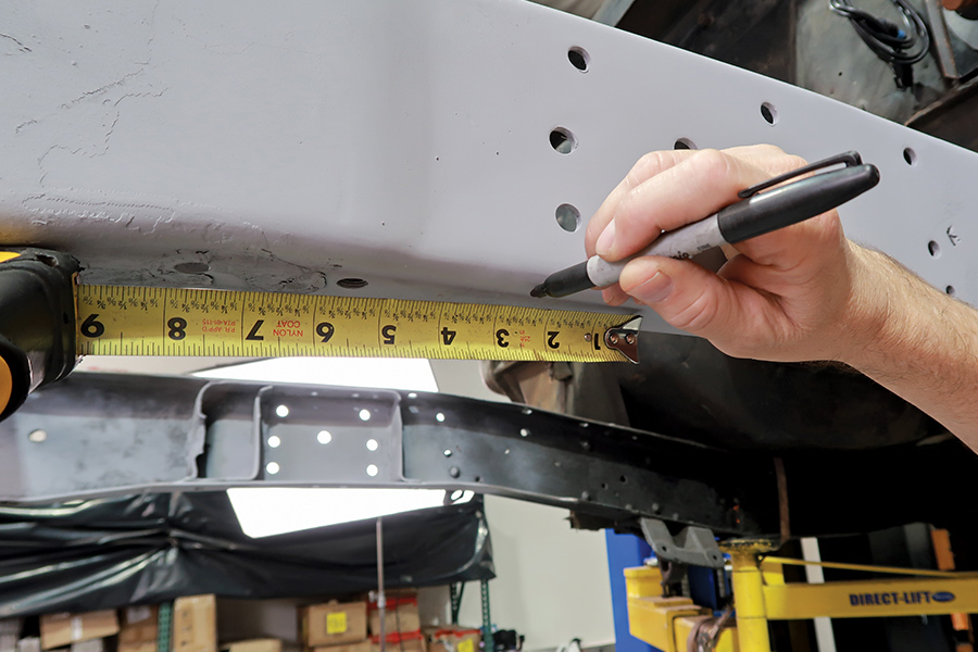 closeup of yellow tape measurer and hand holding black marker up to crossmember