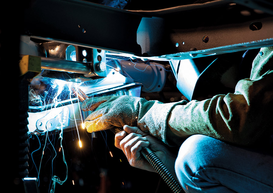 person wearing a welding helmet tacking the Panhard bar bracket in place