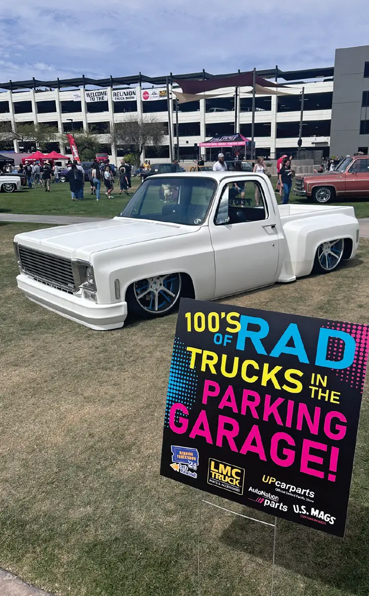 quarter driver side of a white lowriding classic truck parked on a lawn beside show signage