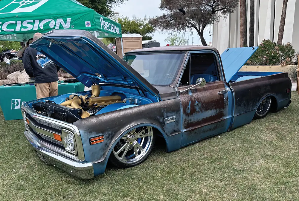 quarter driver side of a metallic blue and patina Chevy C10 with its front hood and bed cover propped open while parked on an event center lawn