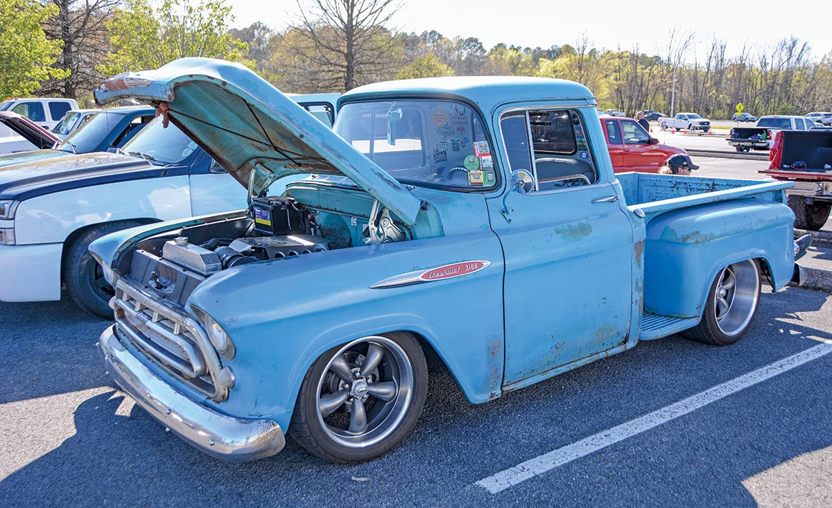 Landscape outdoor close-up photograph angle view of a vintage rusty powder blue colored Chevrolet 3100 truck vehicle parked in a parking lot area nearby other random assorted cars during the day