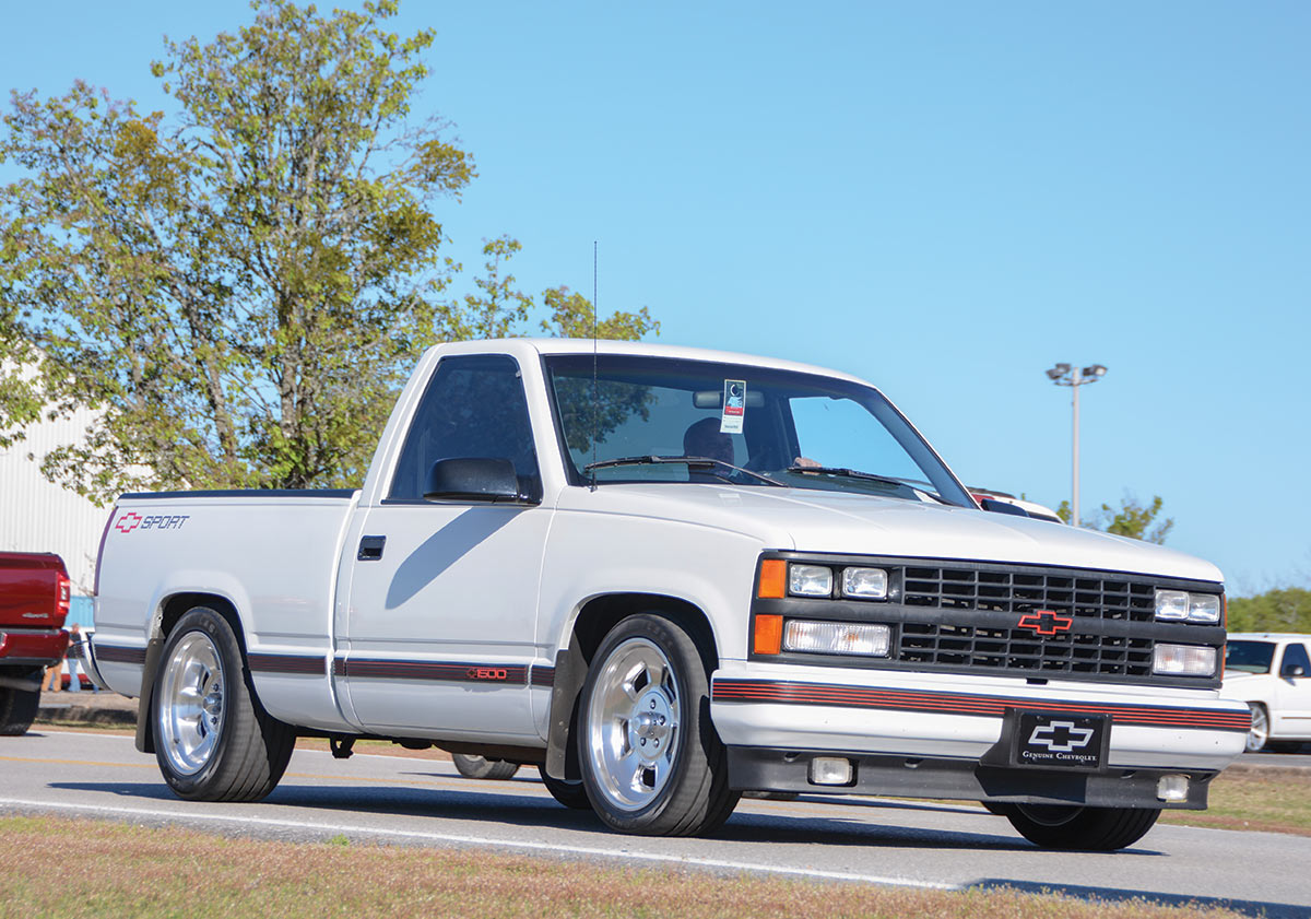 Landscape outdoor close-up photograph angle view of a vintage white Chevrolet Sport truck vehicle with a man driving the car on a road during the day