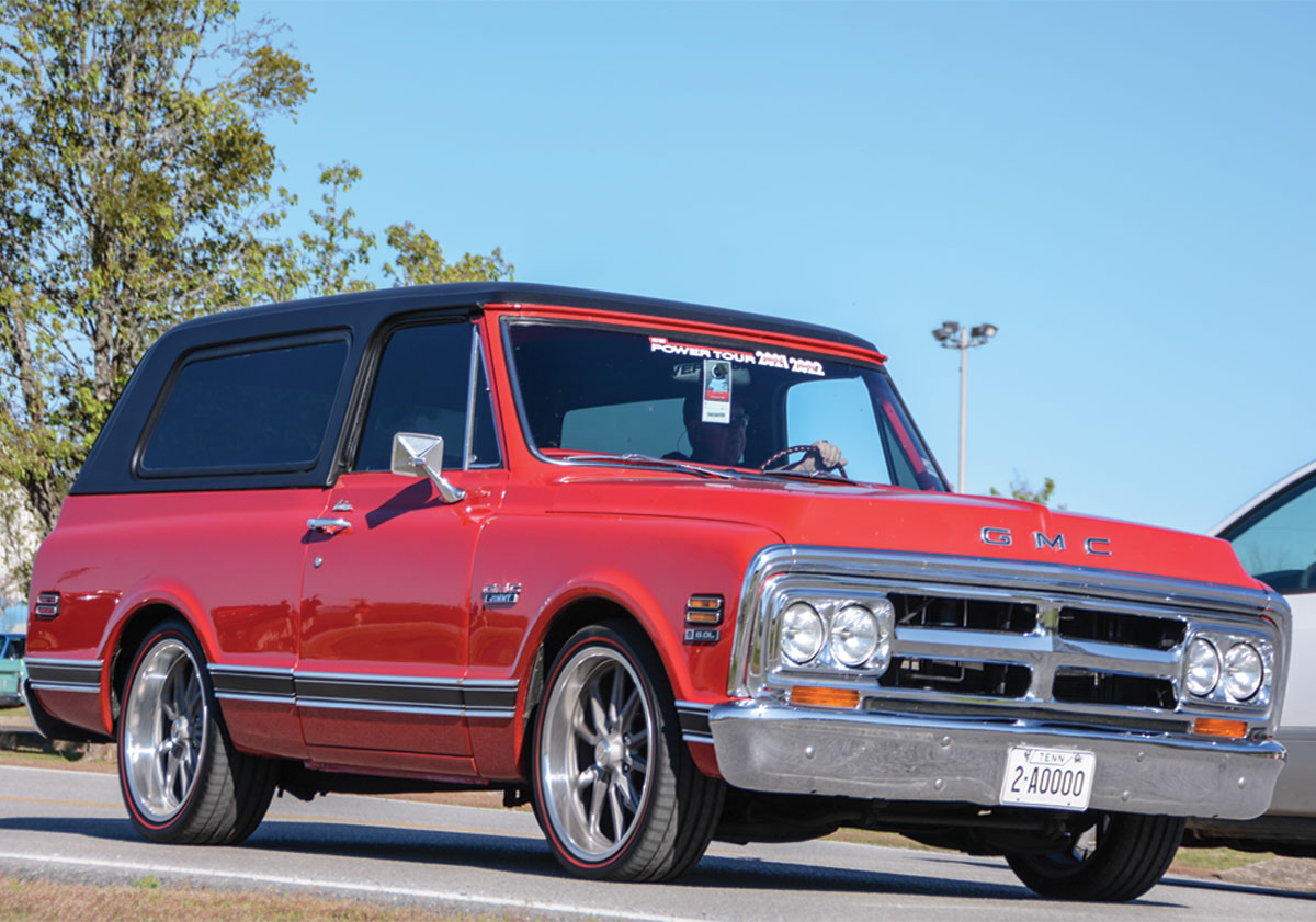 Landscape outdoor close-up photograph angle view of a vintage red GMC truck vehicle with a man driving the car on a road during the day